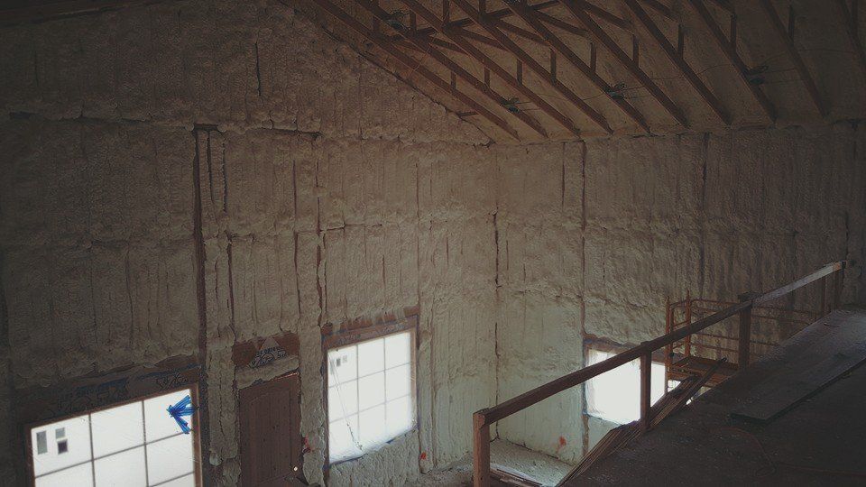 Interior of a building with spray foam insulation on walls and ceiling, windows and a stairway visible.
