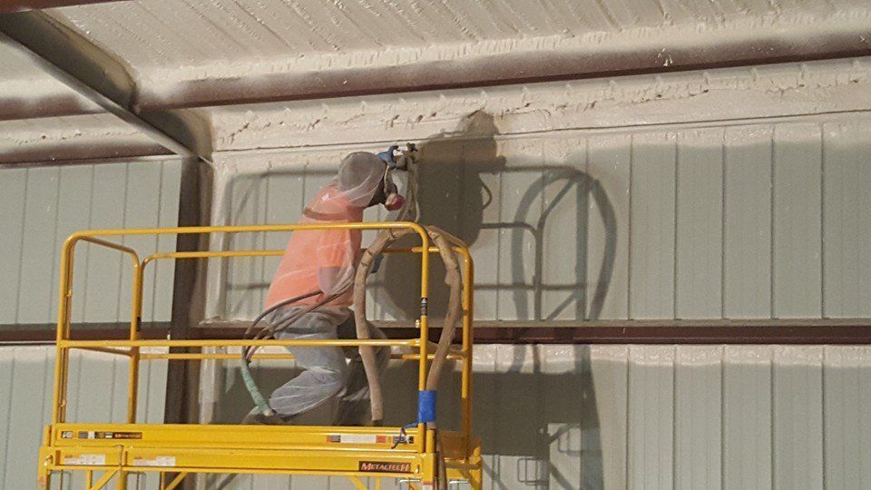 Person on a lift sprays insulation on a wall inside a building.