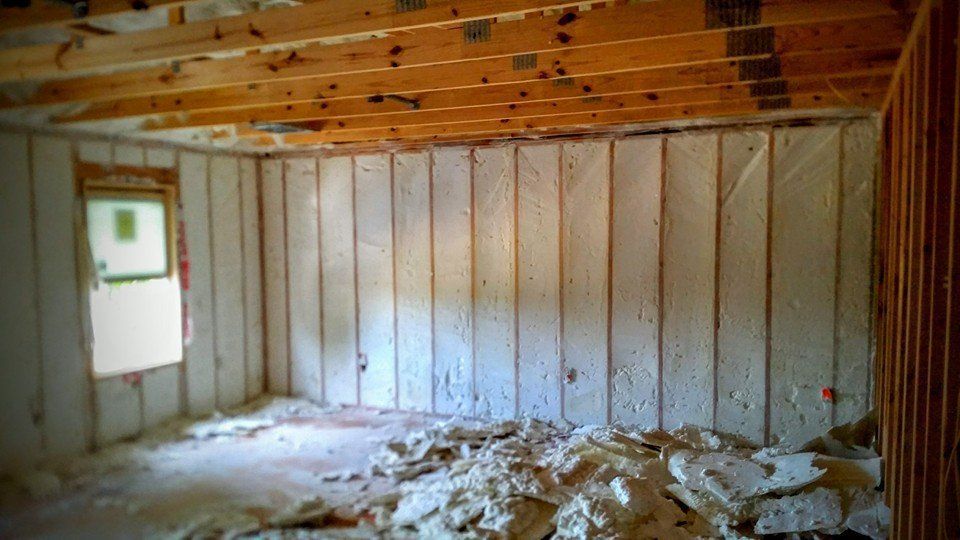 Interior view of a room under construction with exposed wooden beams, white wall panels, and debris on the floor.