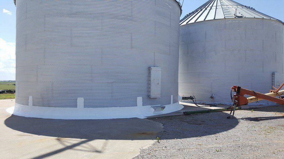 Two silver grain silos on a concrete base against a bright sky.
