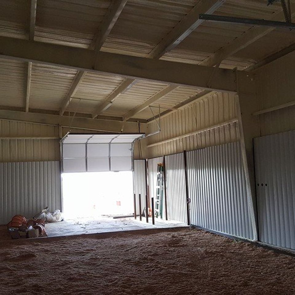 Interior of a building with corrugated metal walls, an open garage door, and spray foam insulation.