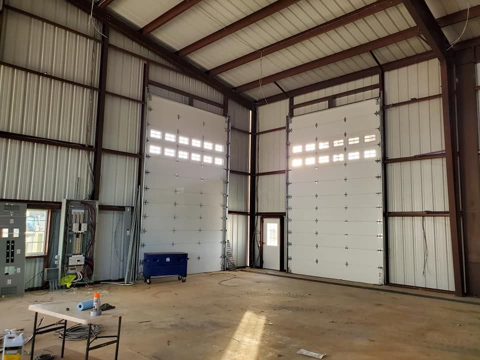 Interior of a large metal building with two large garage doors, a small door, and a table with tools.