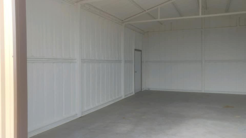 Empty, white-walled storage unit with a concrete floor and a closed door in the back.