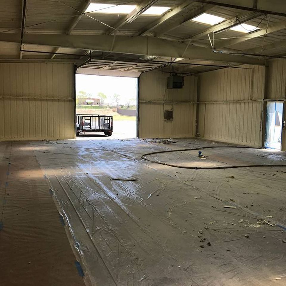 Empty industrial warehouse with open bay door, spray foam insulation, and concrete floor.