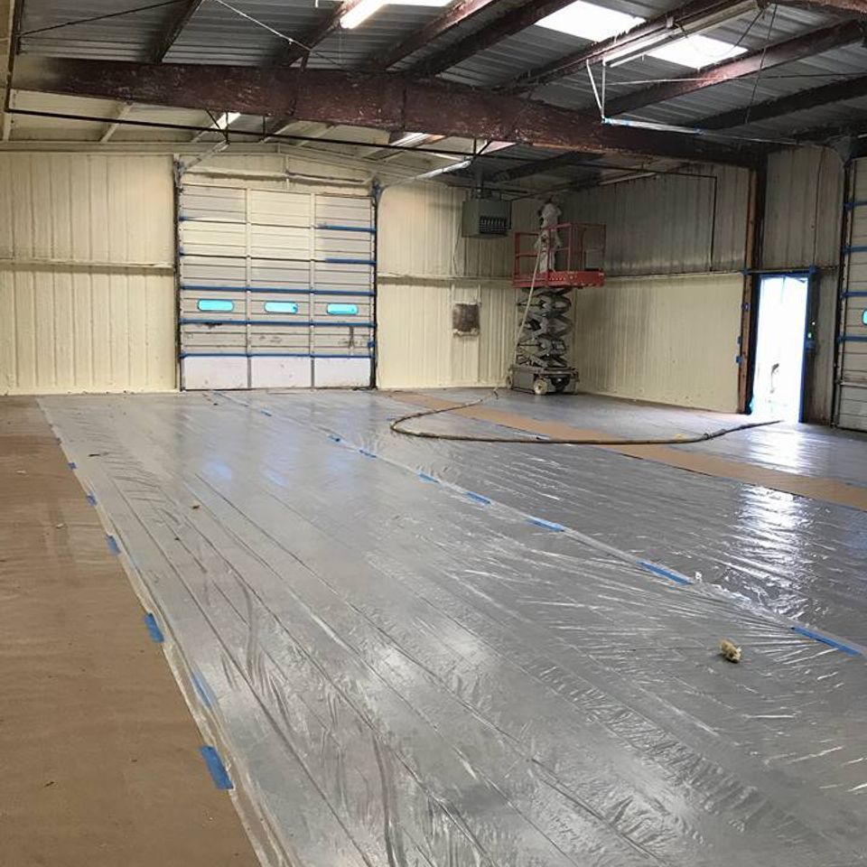 Warehouse interior during construction; floor covered in plastic, walls insulated, worker on a lift.