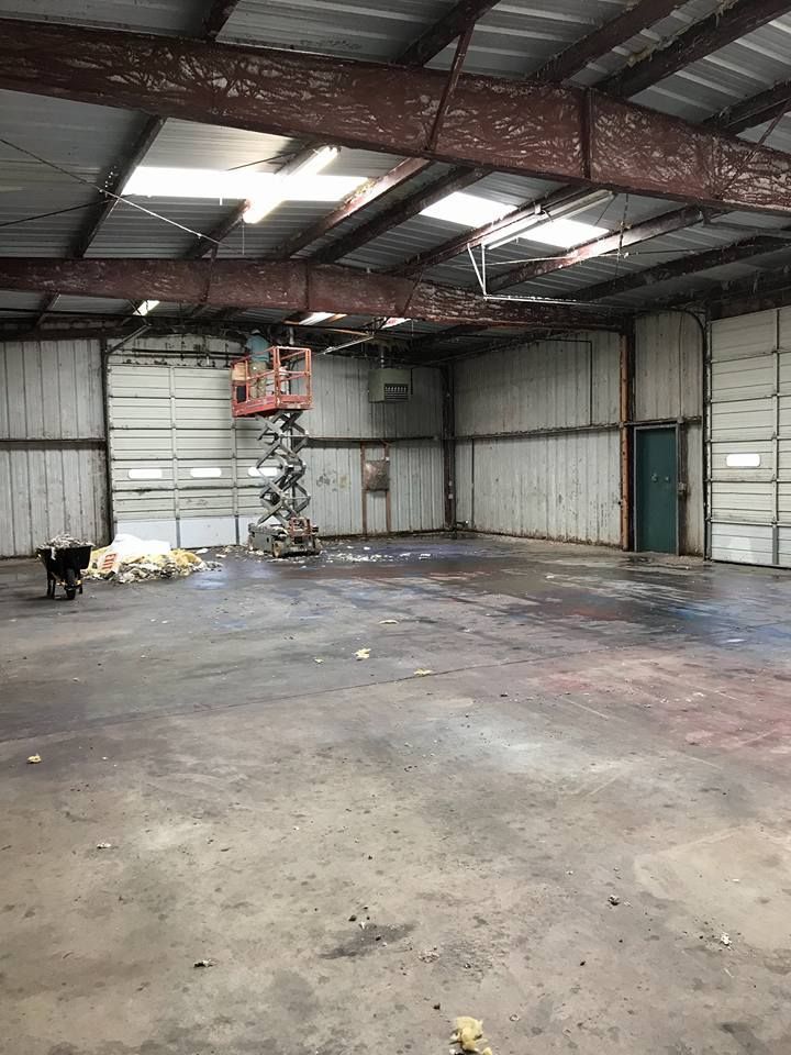 Interior of a large, empty metal building with a scissor lift, two garage doors, and a green door.