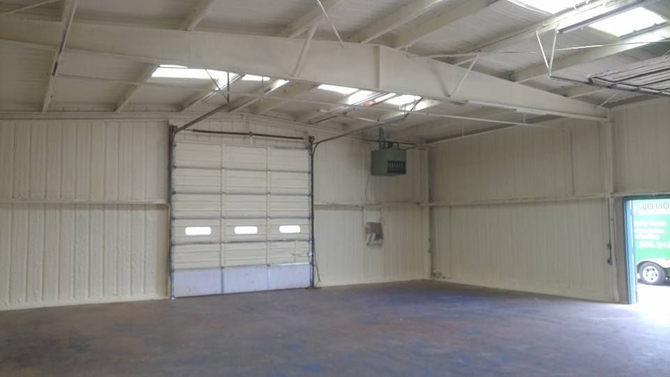 Empty warehouse interior with insulated walls and ceiling, a closed garage door, and an open side door.