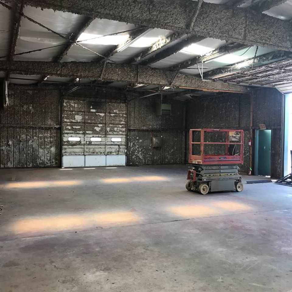 Interior of a large, empty warehouse with a scissor lift, two garage doors, and a green door.