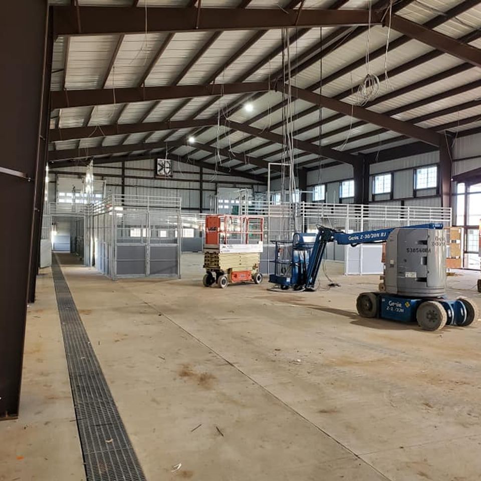 Interior of a large unfinished building with metal beams, concrete floor, and machinery.