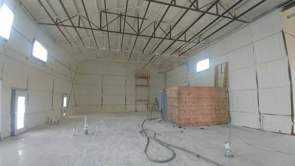 Interior of a large, empty commercial building with spray foam insulation on walls and ceiling.