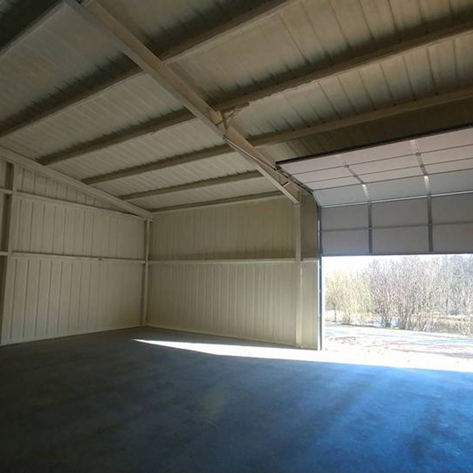 Empty metal storage building interior with open doorway and concrete floor.