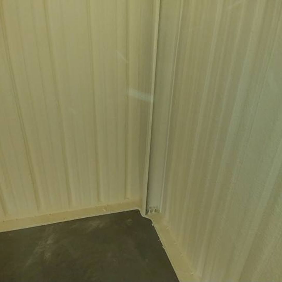 Corner of a room with ribbed, light-colored walls and a dark gray floor.