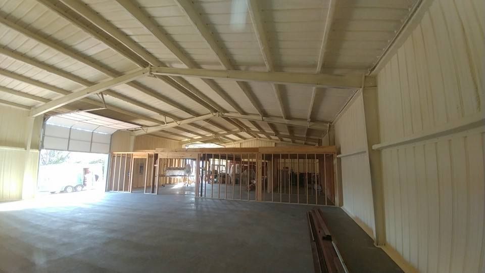 Interior view of a large metal building under construction, with exposed beams and a concrete floor.