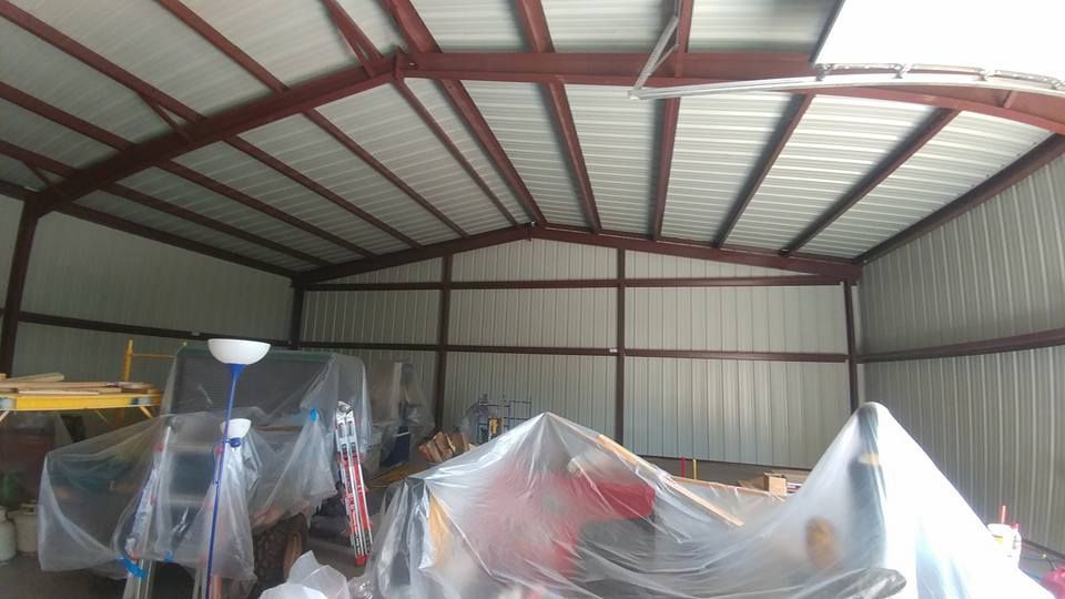 Interior of a metal building with red framing and white walls and ceiling. Tools and objects covered with plastic.