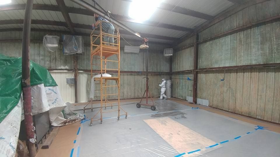 Workers in protective suits and on scaffolding inside a metal warehouse during construction.