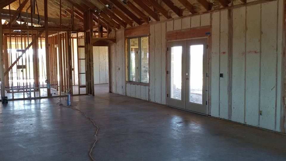 Interior of a building under construction, with exposed wooden framing, concrete floor, and windows.