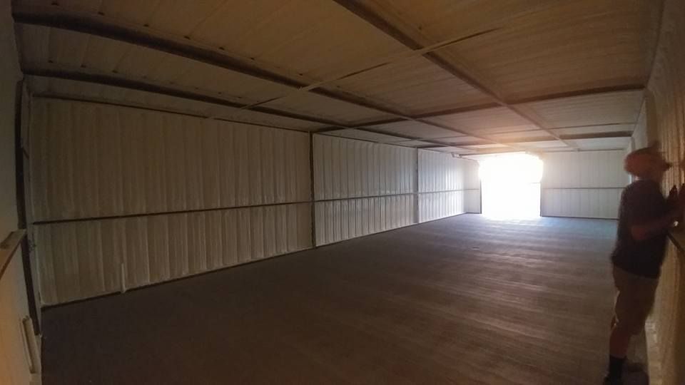 Inside view of an empty white warehouse, with a man standing near the right wall and a bright doorway at the end.