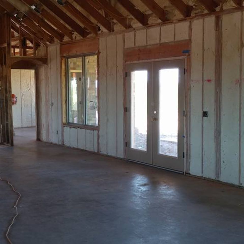 Interior of a building under construction, showing concrete floor, framed walls, a window, and double doors.