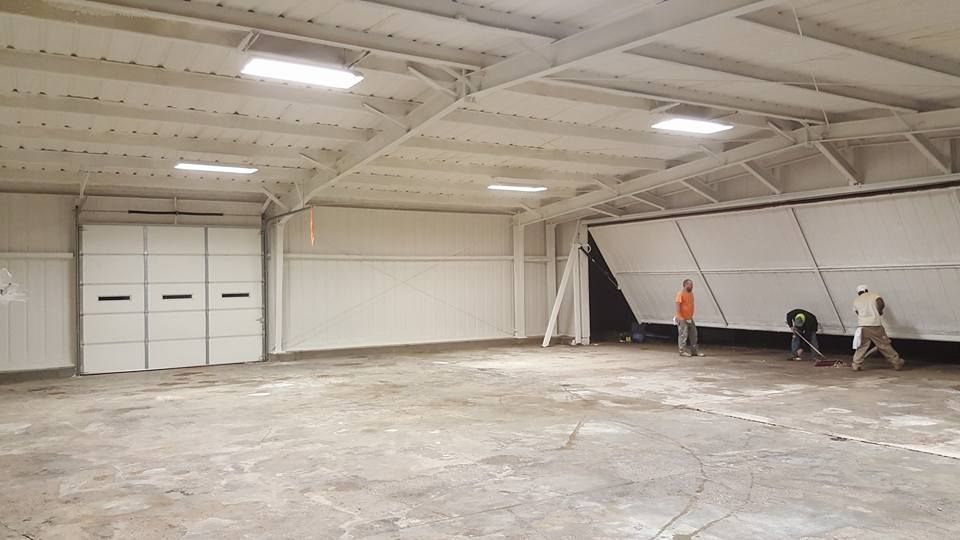 Interior of a white warehouse with open folding door, three workers, and a concrete floor.