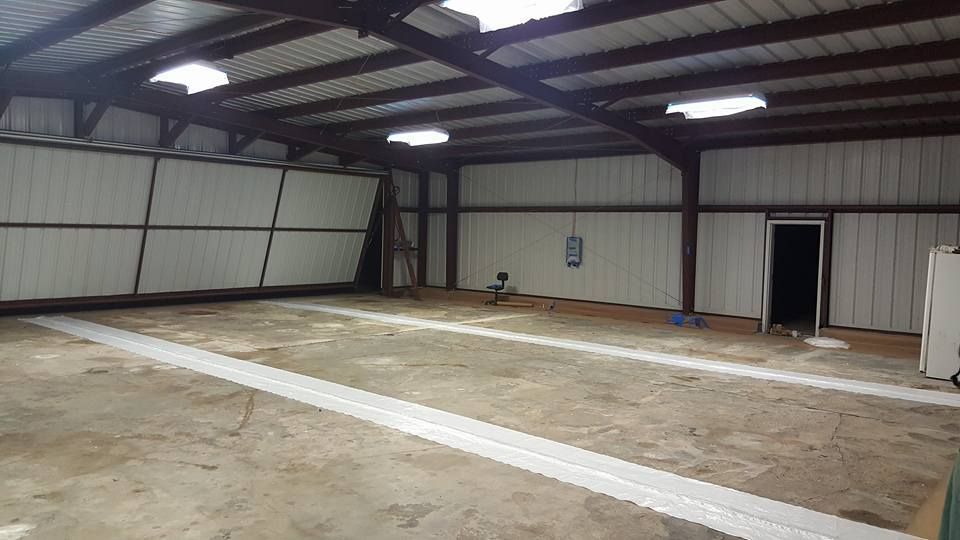 Empty metal warehouse with concrete floor, white walls, and overhead lights.
