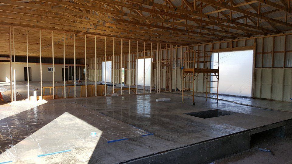 Interior of a building under construction, with exposed wood framing, concrete floor, and windows.
