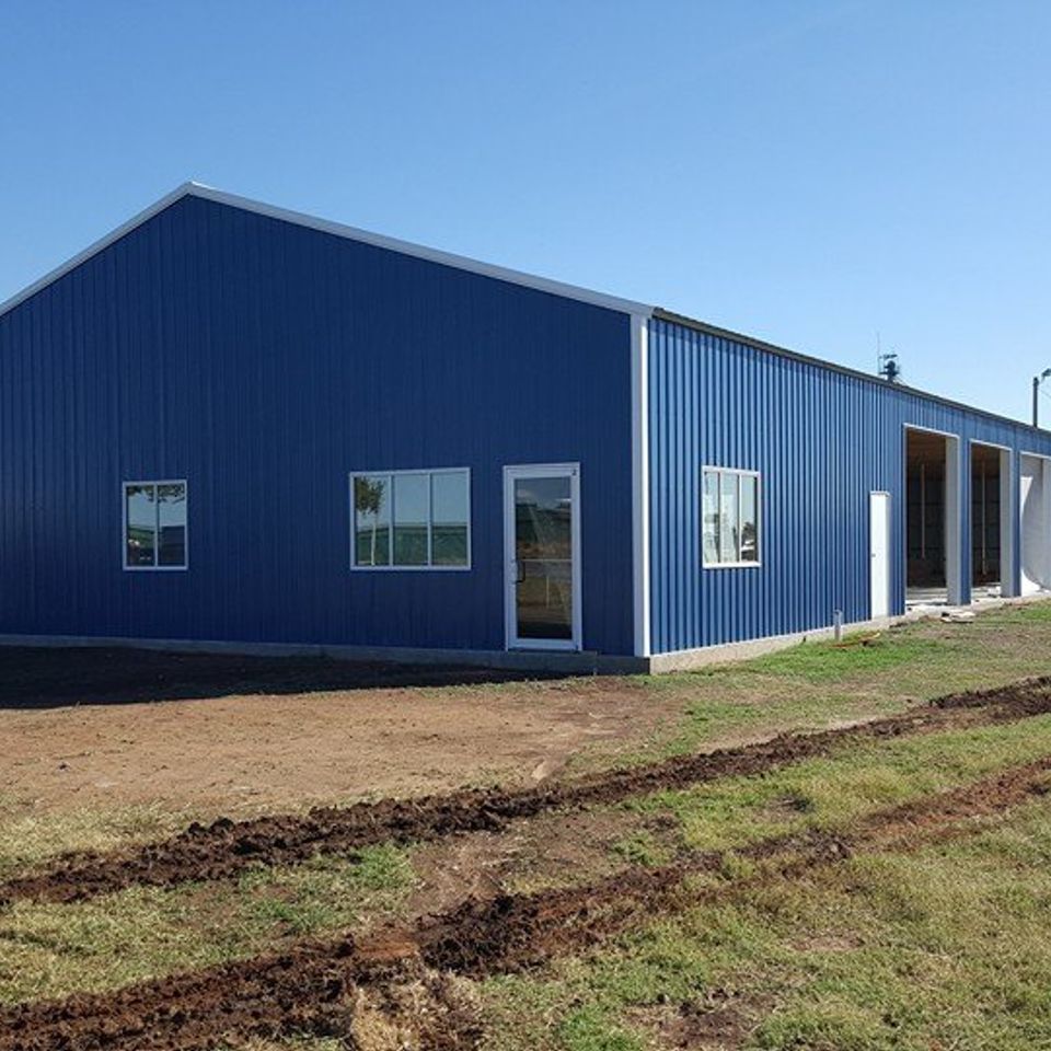 Blue metal building with white trim, windows, and large garage doors, on a grassy field.