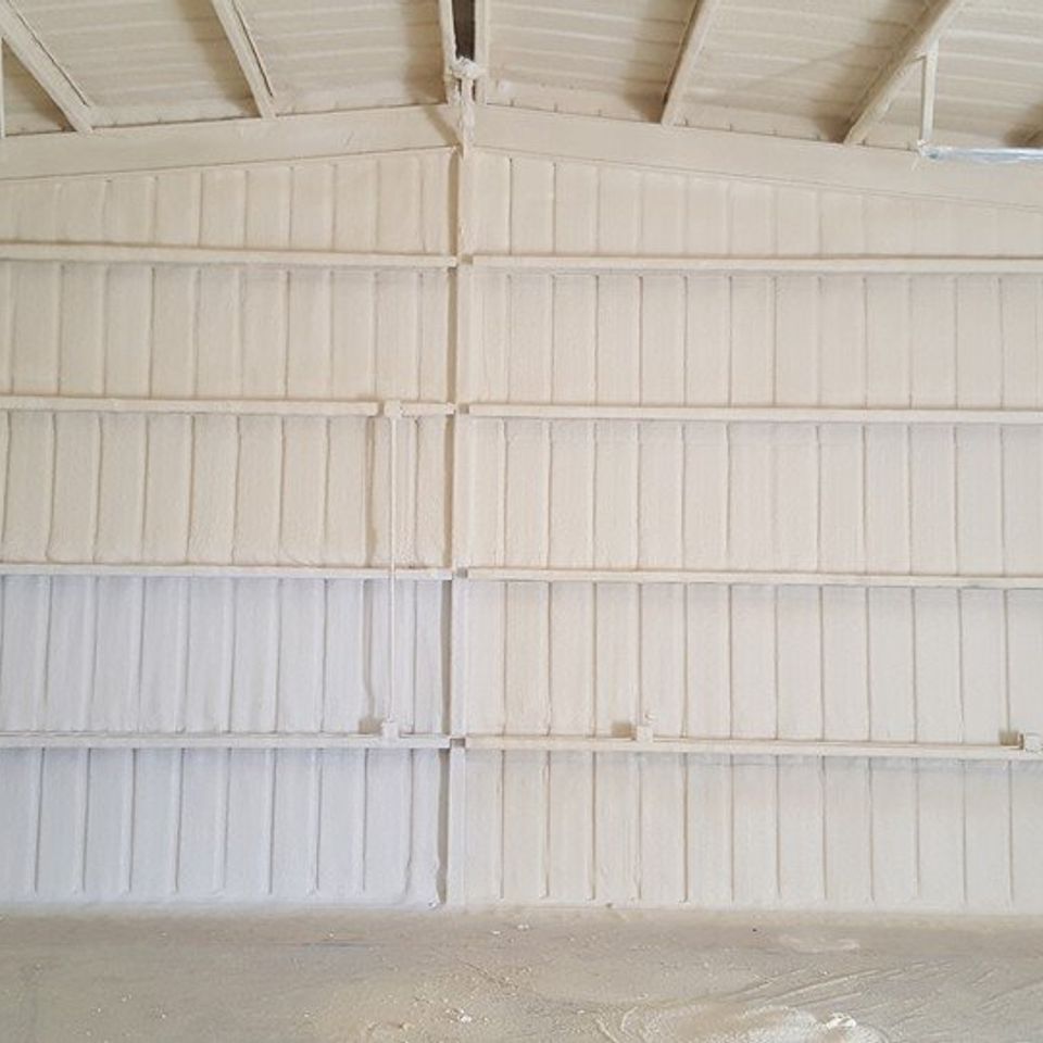 Interior view of a metal building with spray foam insulation on walls and ceiling; beige color.