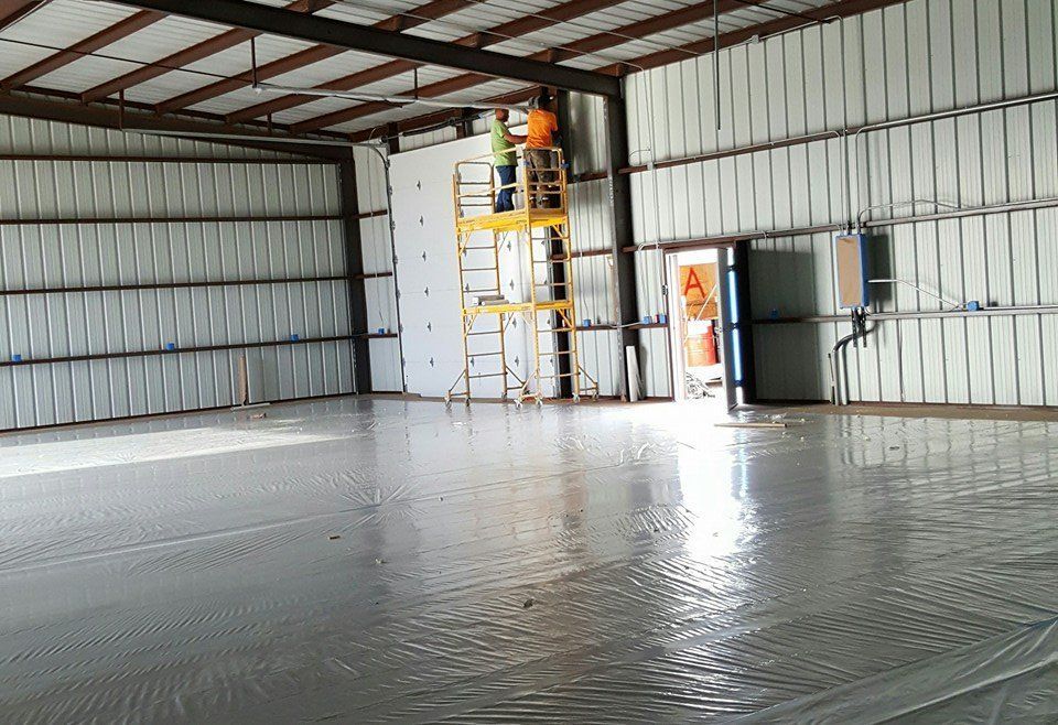 Workers on a lift installing insulation in a metal warehouse with a wet concrete floor.