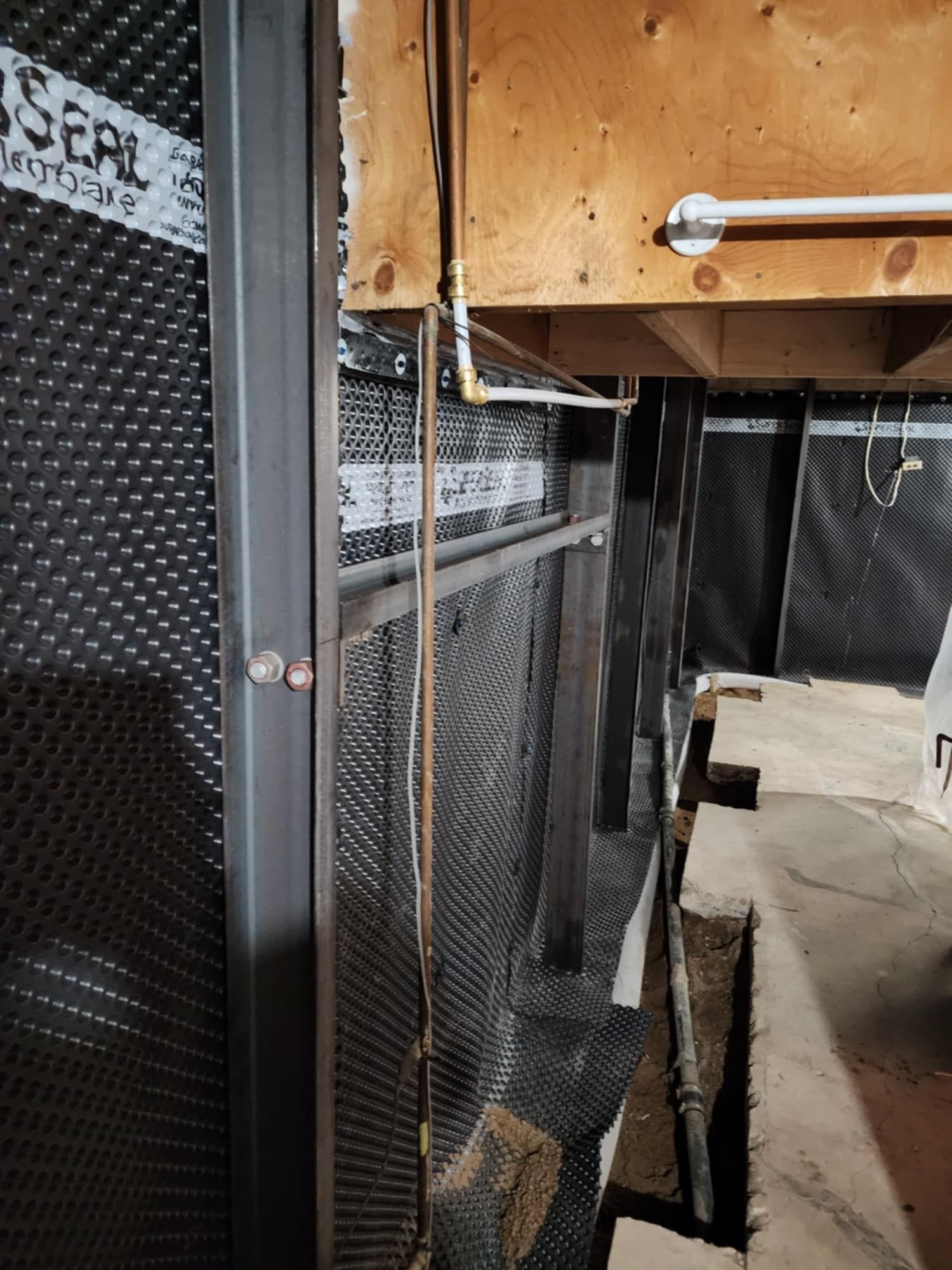 Basement interior showing a black dimpled drainage membrane, metal beams.