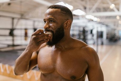 Shirtless man wiping sweat in a gym with basketball courts in the background