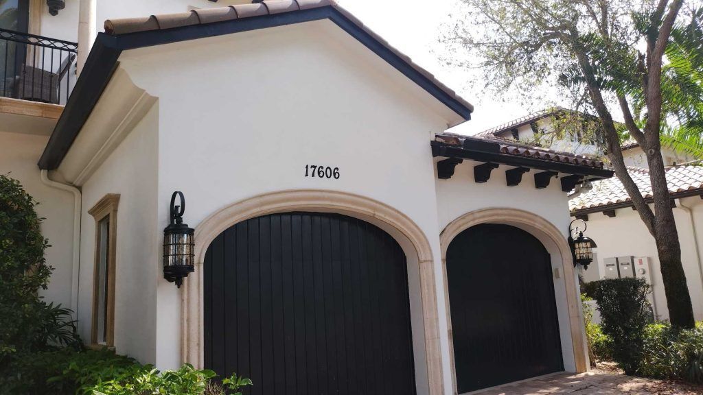 A white house with black garage doors and the number 17bx on the side
