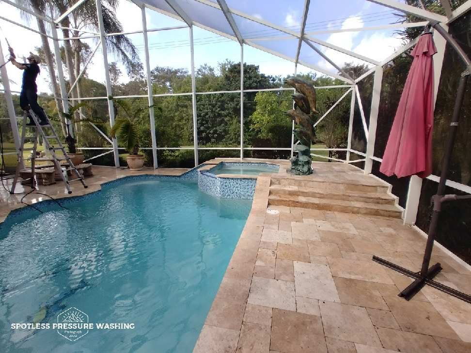 A man is cleaning a screened in pool with a pink umbrella.
