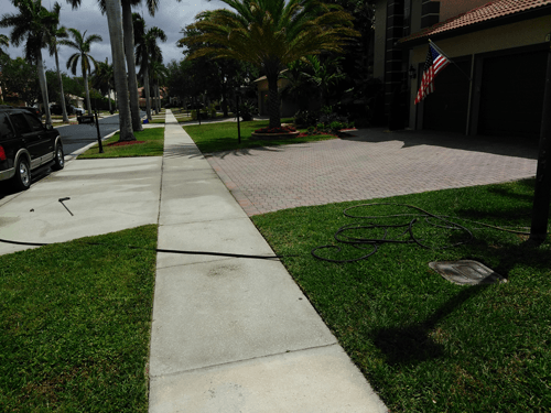 A sidewalk in front of a house with a hose attached to it