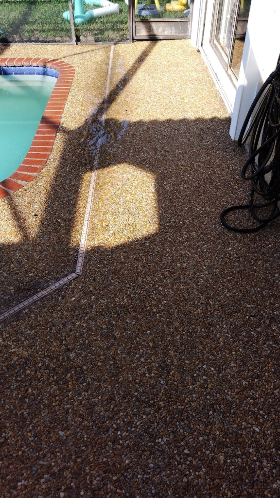 A patio with a pool in the background and a hose on the ground.