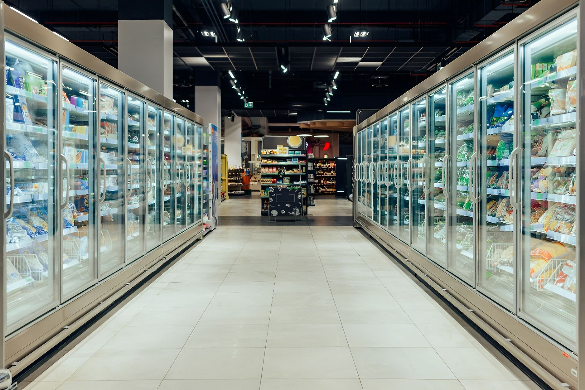 Rows of freezer cases in a grocery store aisle, lit with white light, filled with products.