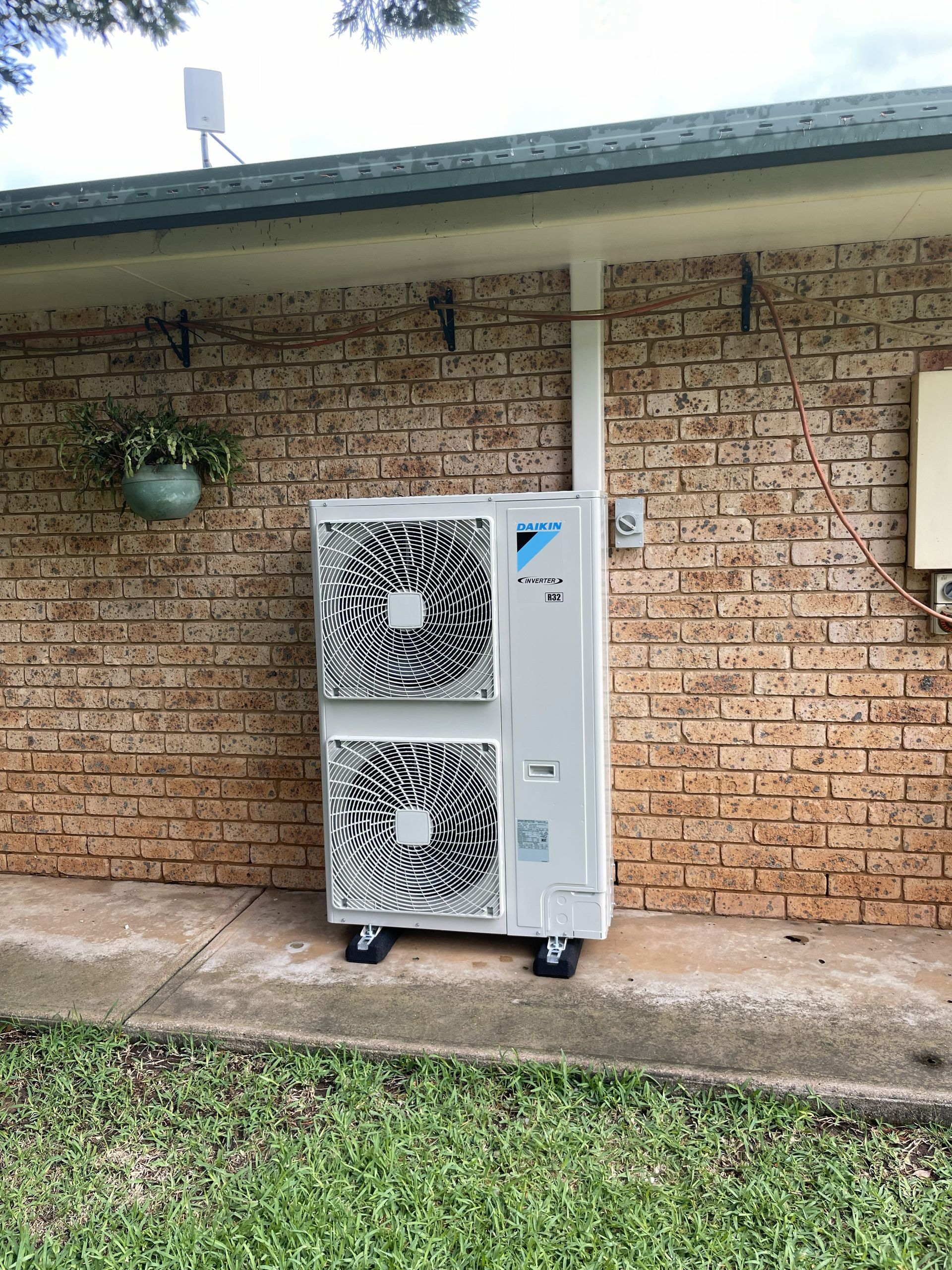 Air conditioning unit on wheels against a brick wall, pipe extending upwards.