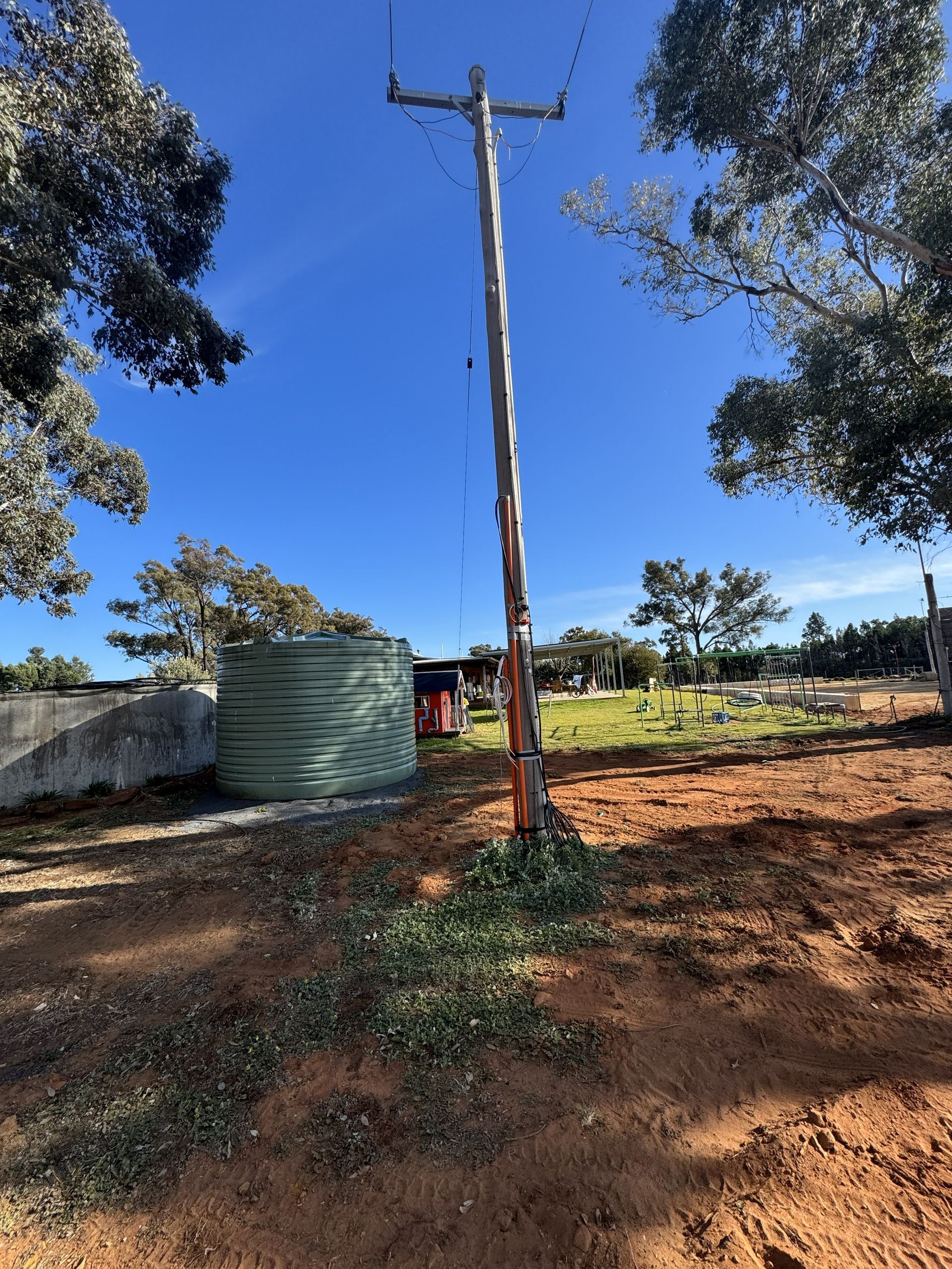 Wooden utility pole in an open field, with a water tank and blue sky in the background.
