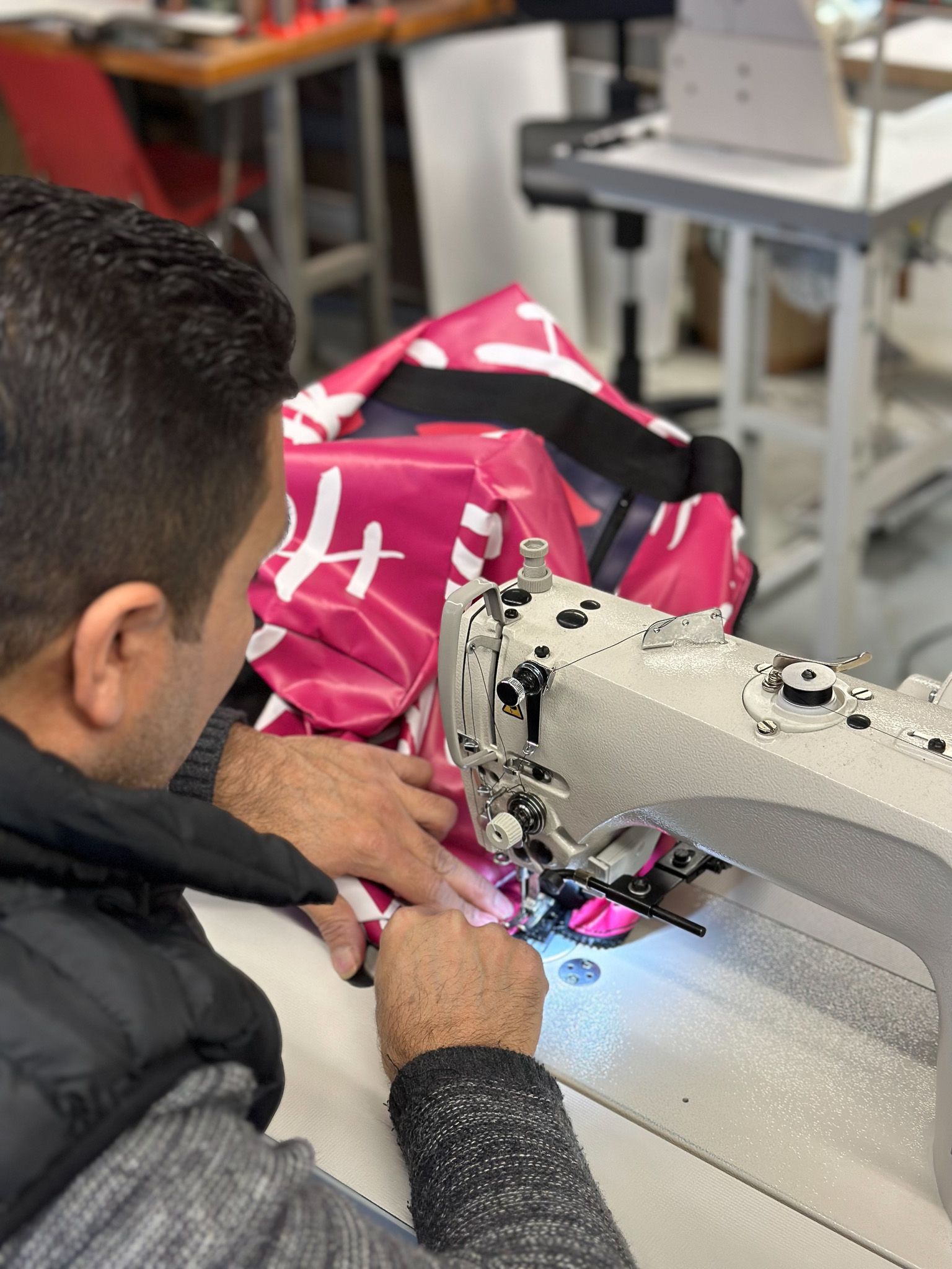 Detailopname van textielbewerking in het Upcycle Lab, met de focus op handen die zorgvuldig stofnaad naaien.