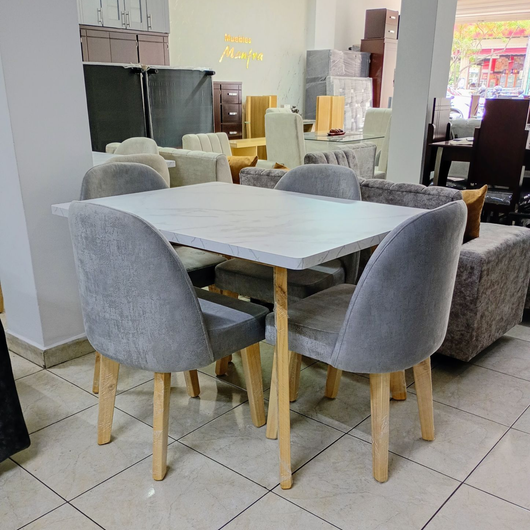 Sillas de comedor tapizadas en gris alrededor de una mesa blanca en una sala de exposición de muebles.