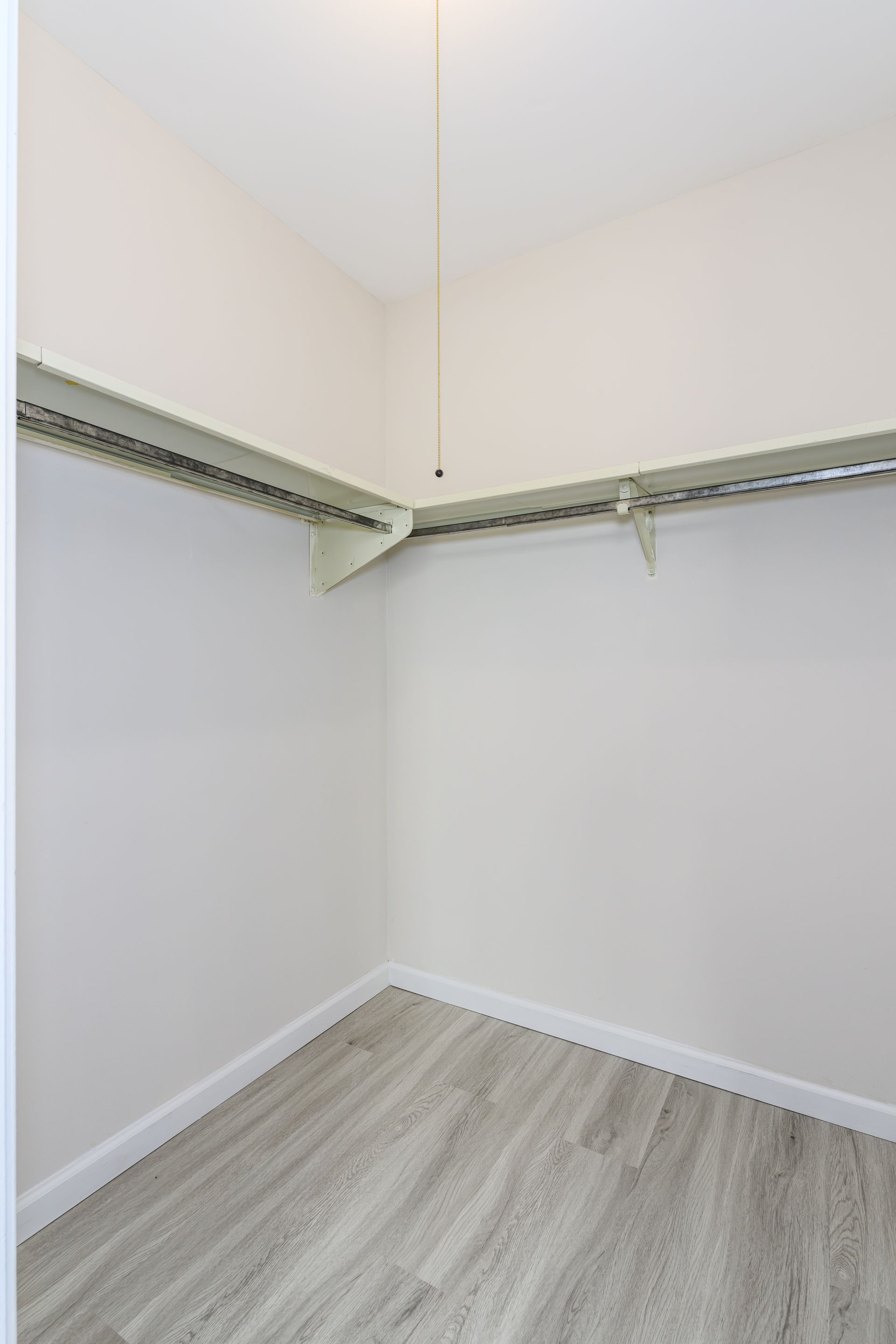 An empty walk in closet with hardwood floors and white walls.