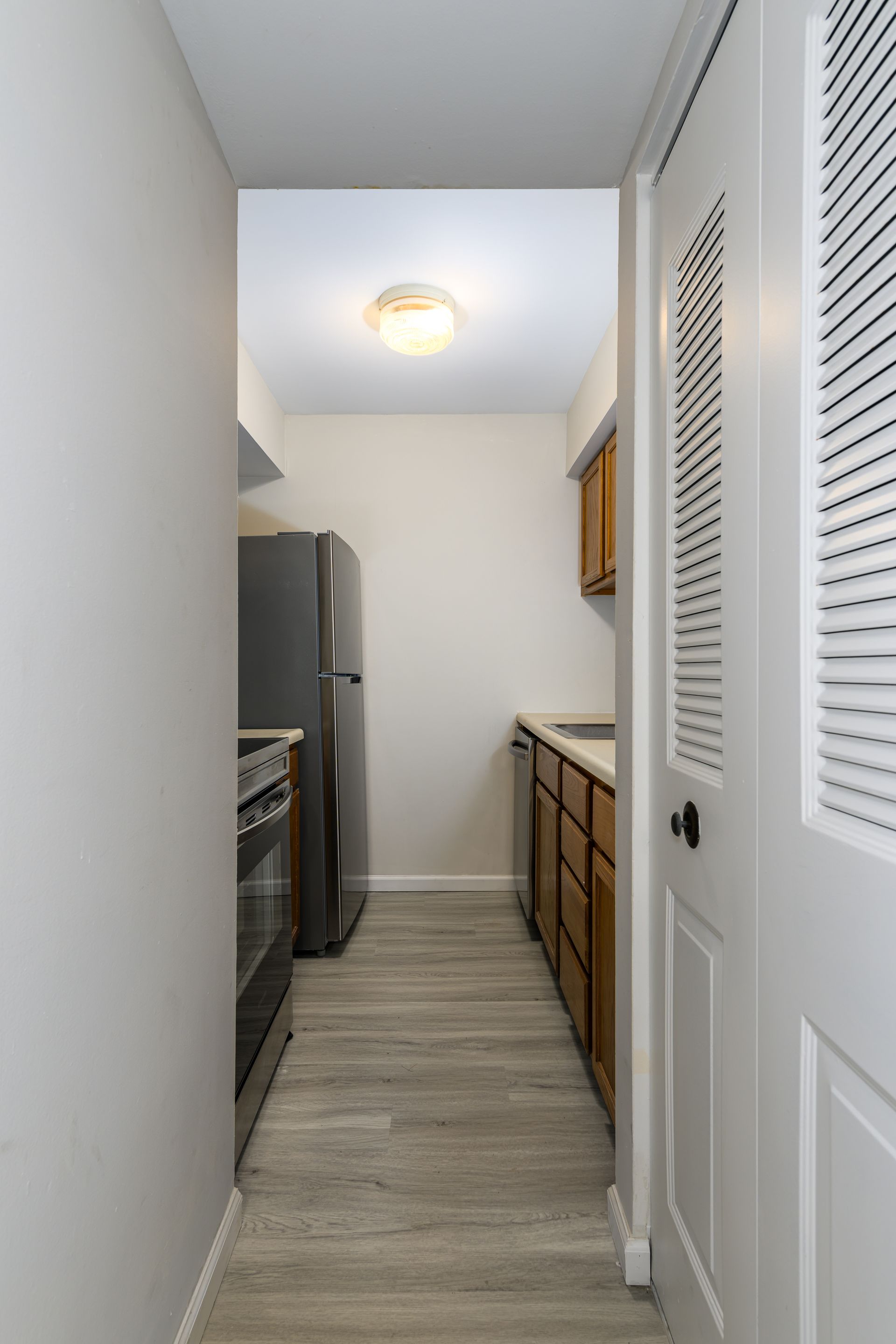 A hallway leading to a kitchen with a refrigerator , stove , and dishwasher.