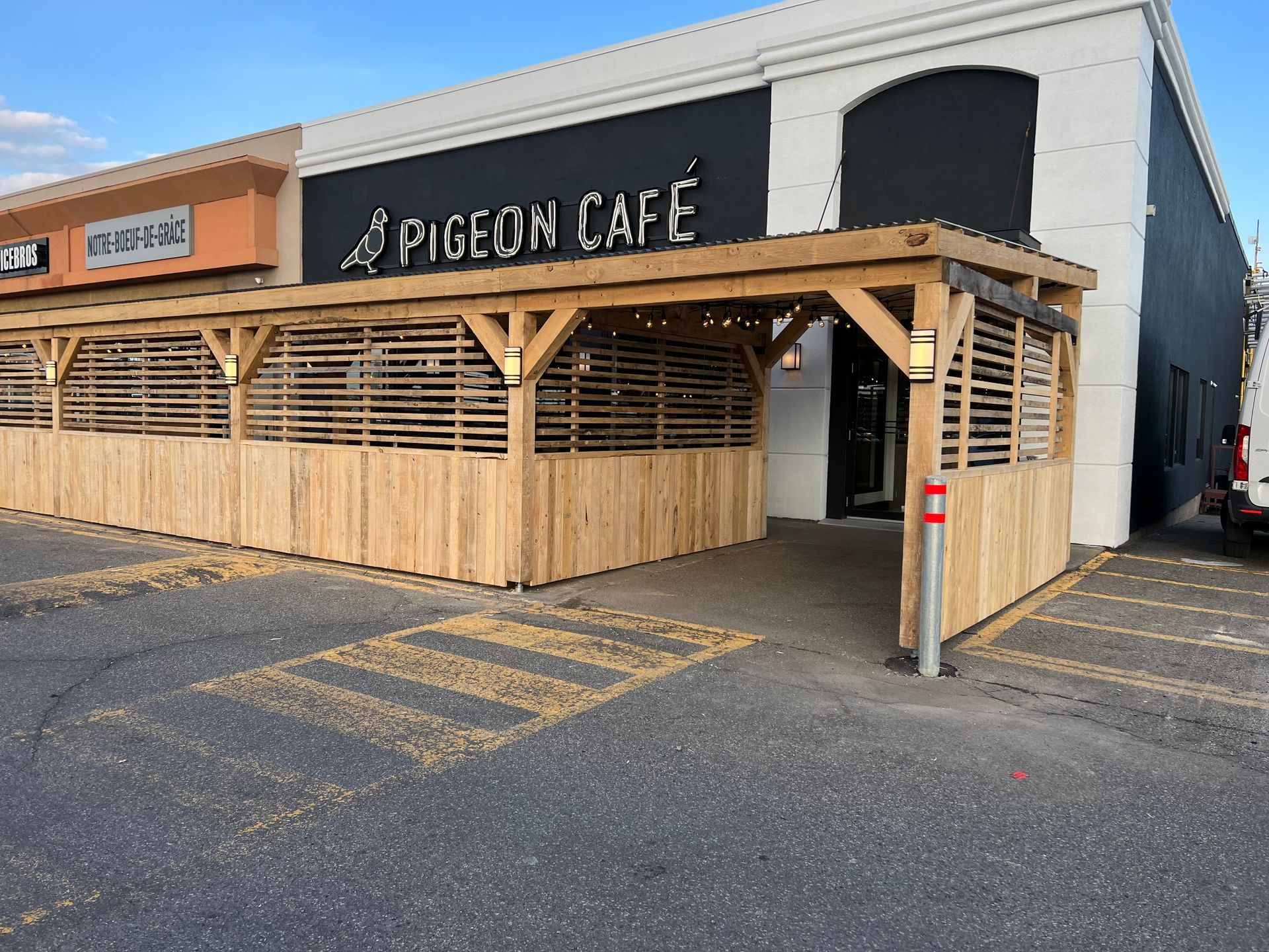 Façade du Pigeon Café avec enseigne noire, auvent en bois et parking vide au crépuscule