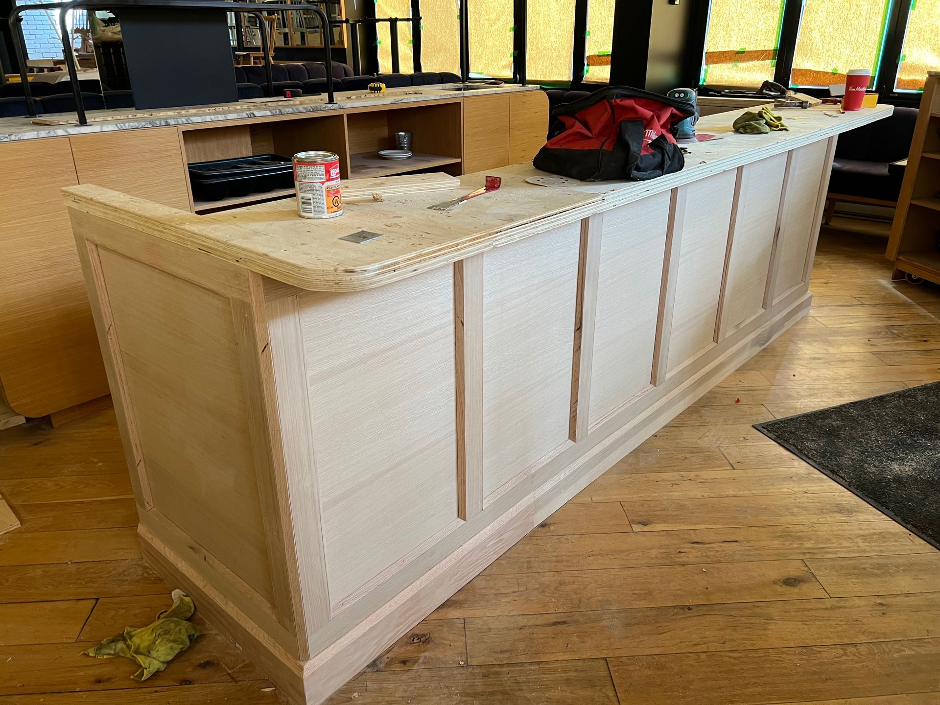 Îlot de cuisine avec placards en bois clair, comptoir en granit et un sac rouge dans une pièce en rénovation