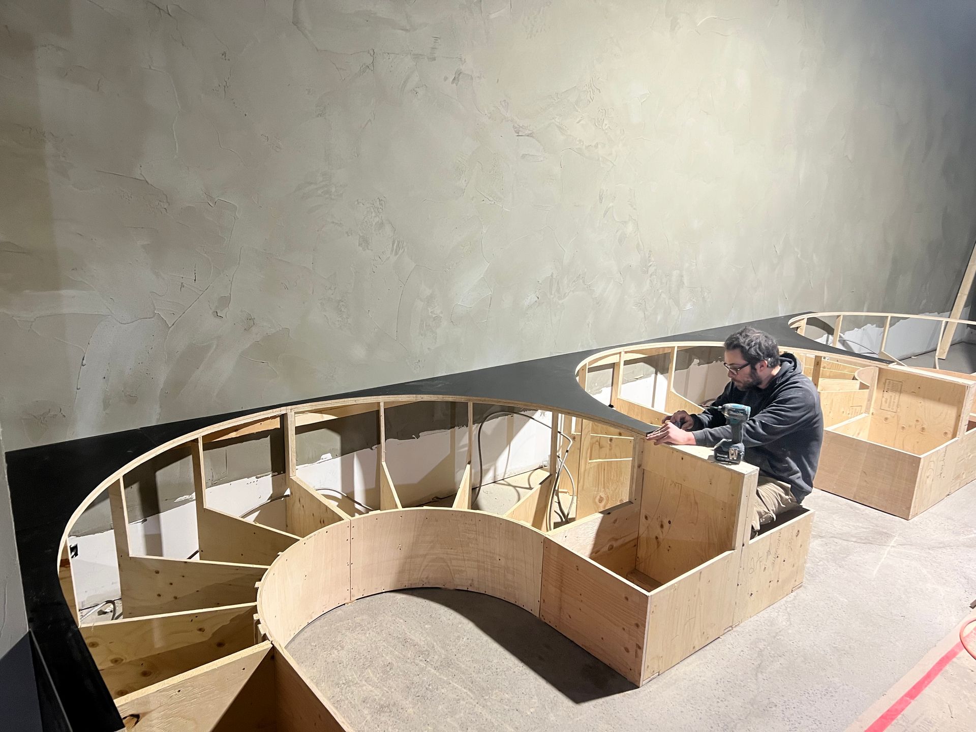 Une personne travaille sur une maquette en carton à grande échelle dans une pièce aux murs en béton.