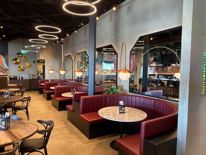 Intérieur de restaurant élégant avec banquettes bordeaux, tables rondes, miroirs et luminaires circulaires au plafond.