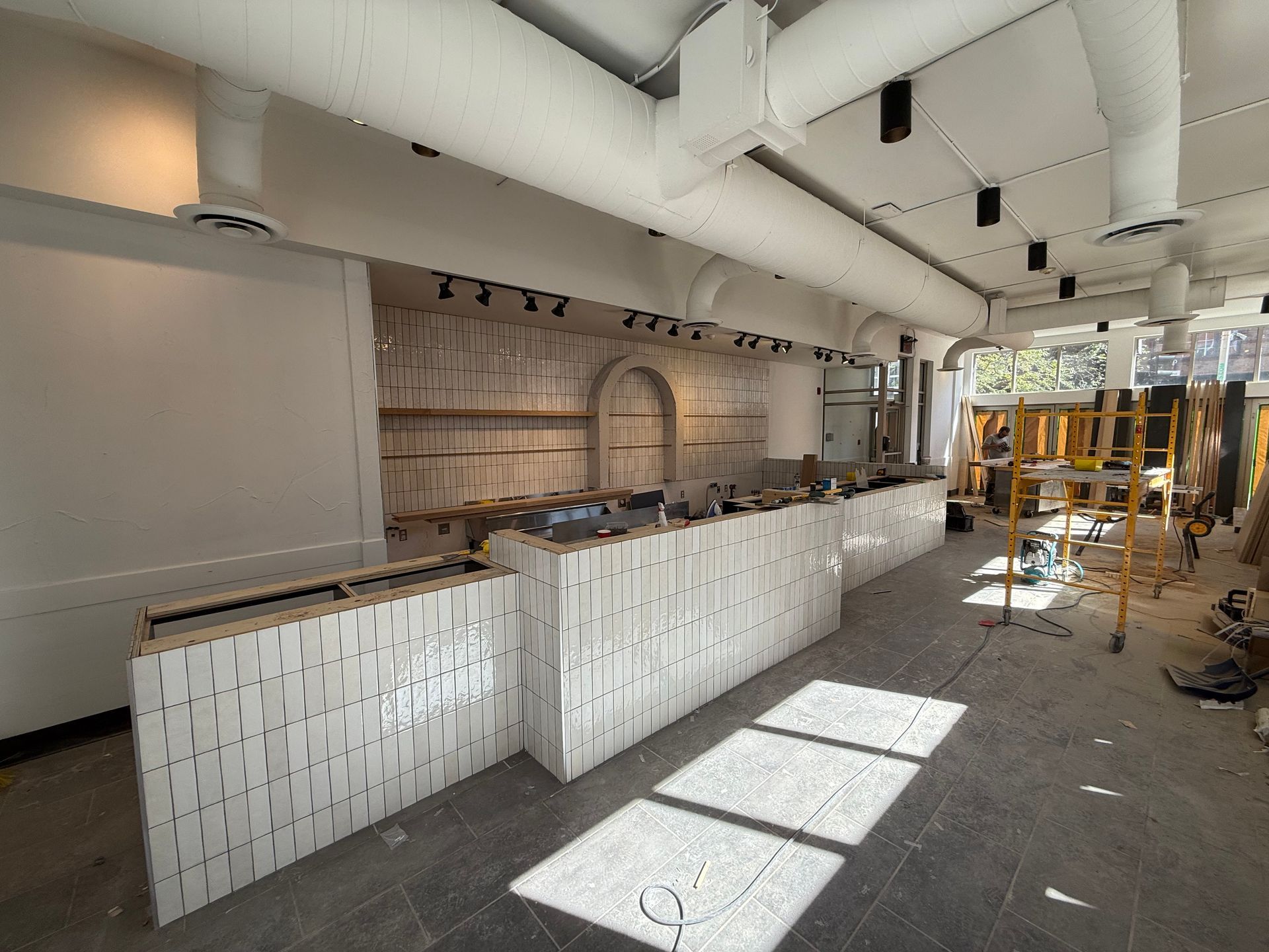 Bar partiellement construit, carrelé de blanc, dans un intérieur moderne avec des échafaudages et des matériaux de construction à proximité.