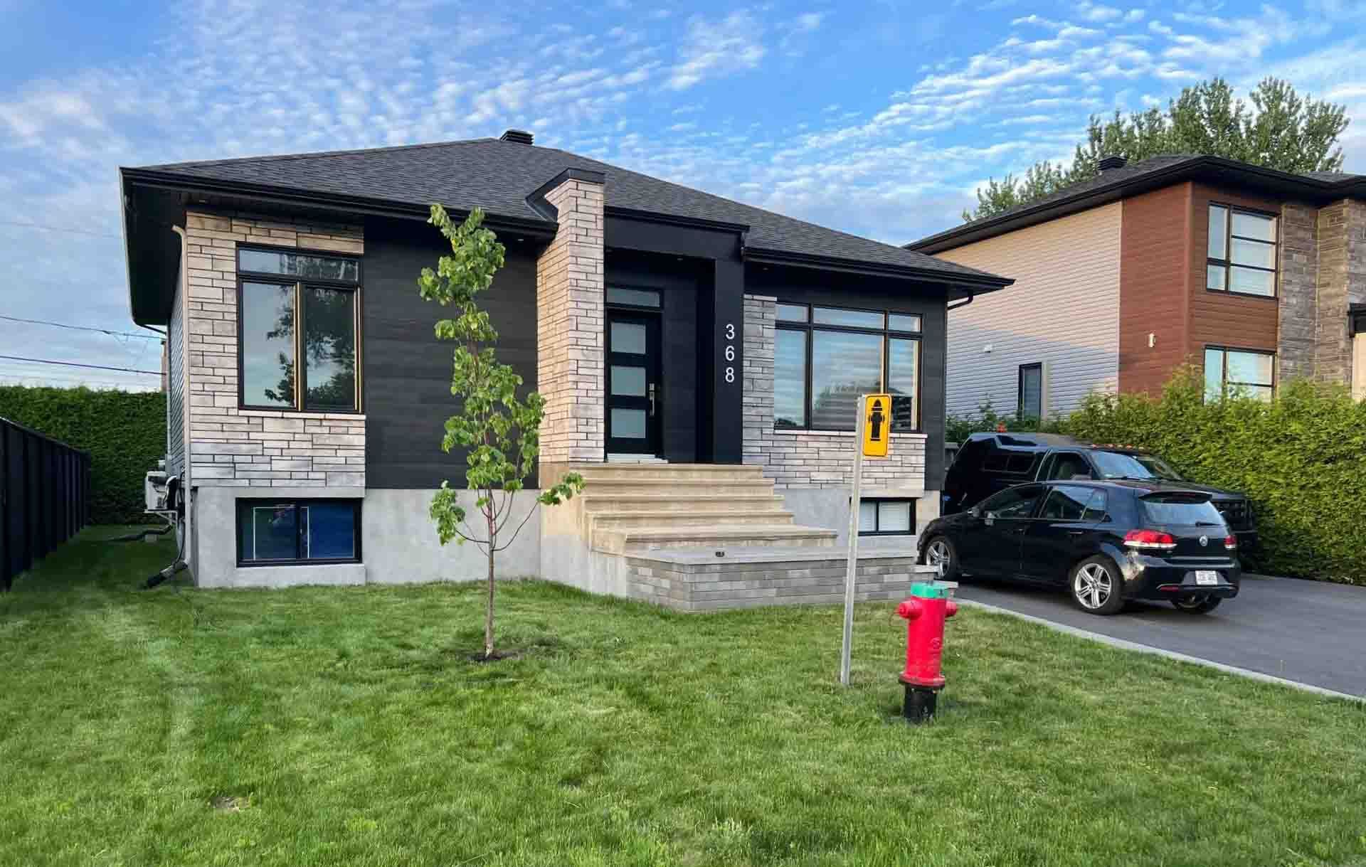 Maison moderne de plain-pied avec perron, pelouse, allée, voiture garée et borne d'incendie rouge.