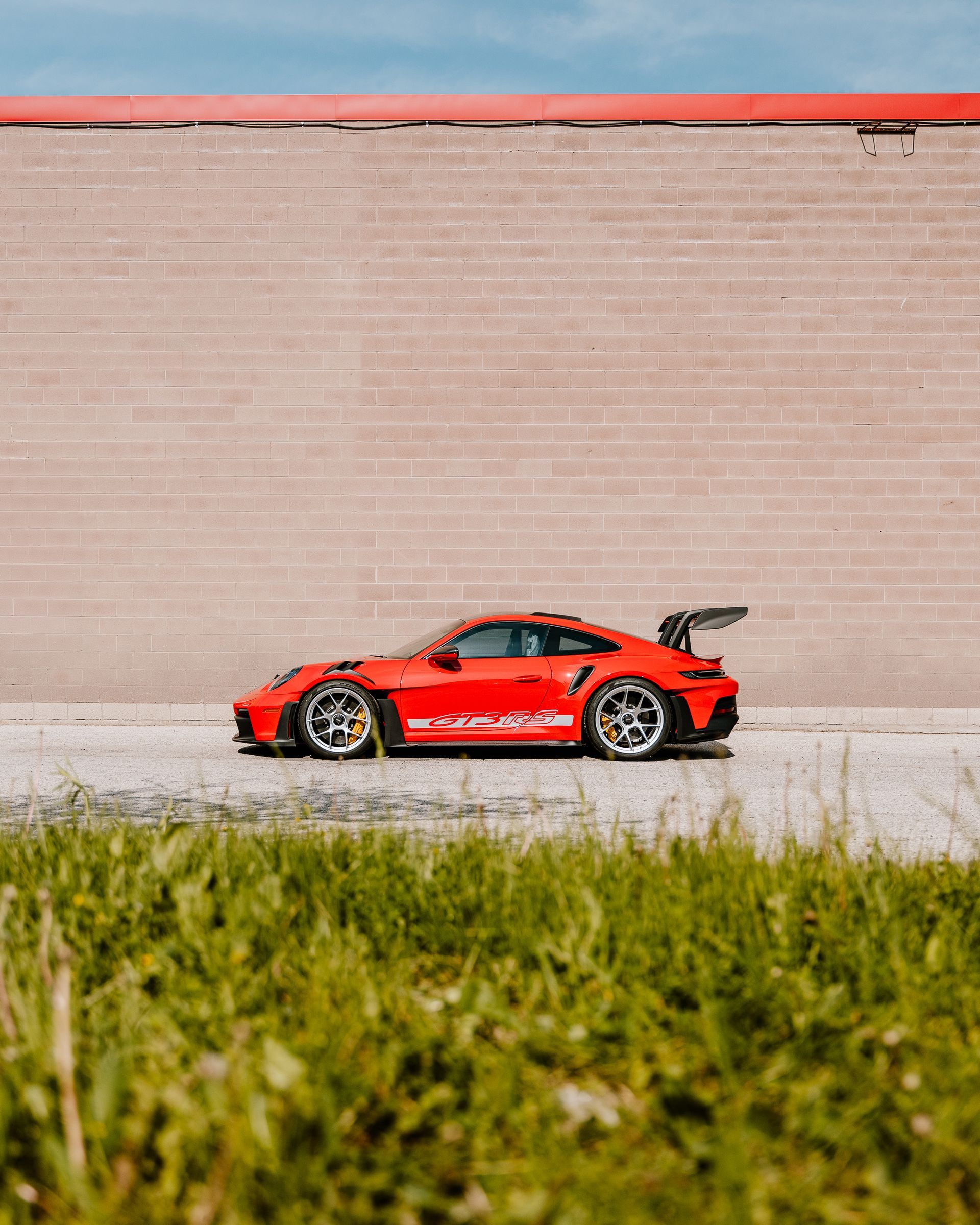 A red porsche 911 gt3 rs is parked on the side of the road in front of a brick wall.