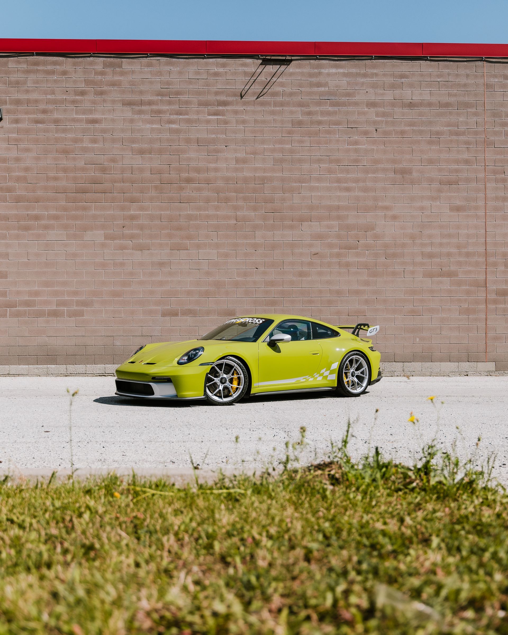 A yellow sports car is parked in front of a brick wall.