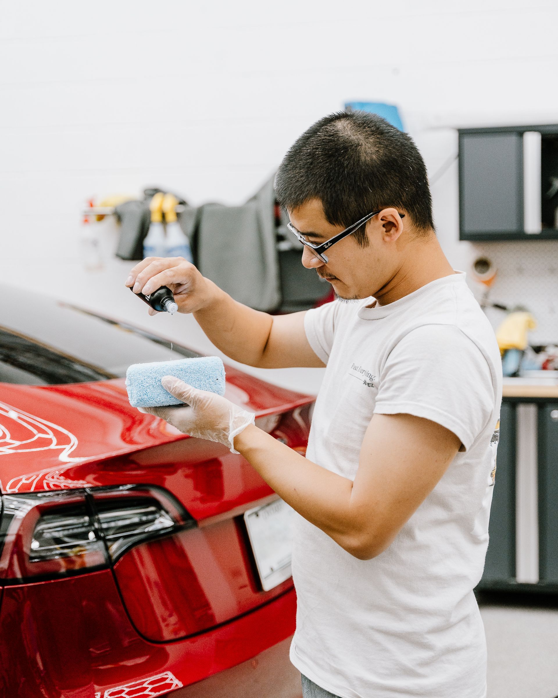 A man is cleaning a red car with a sponge.